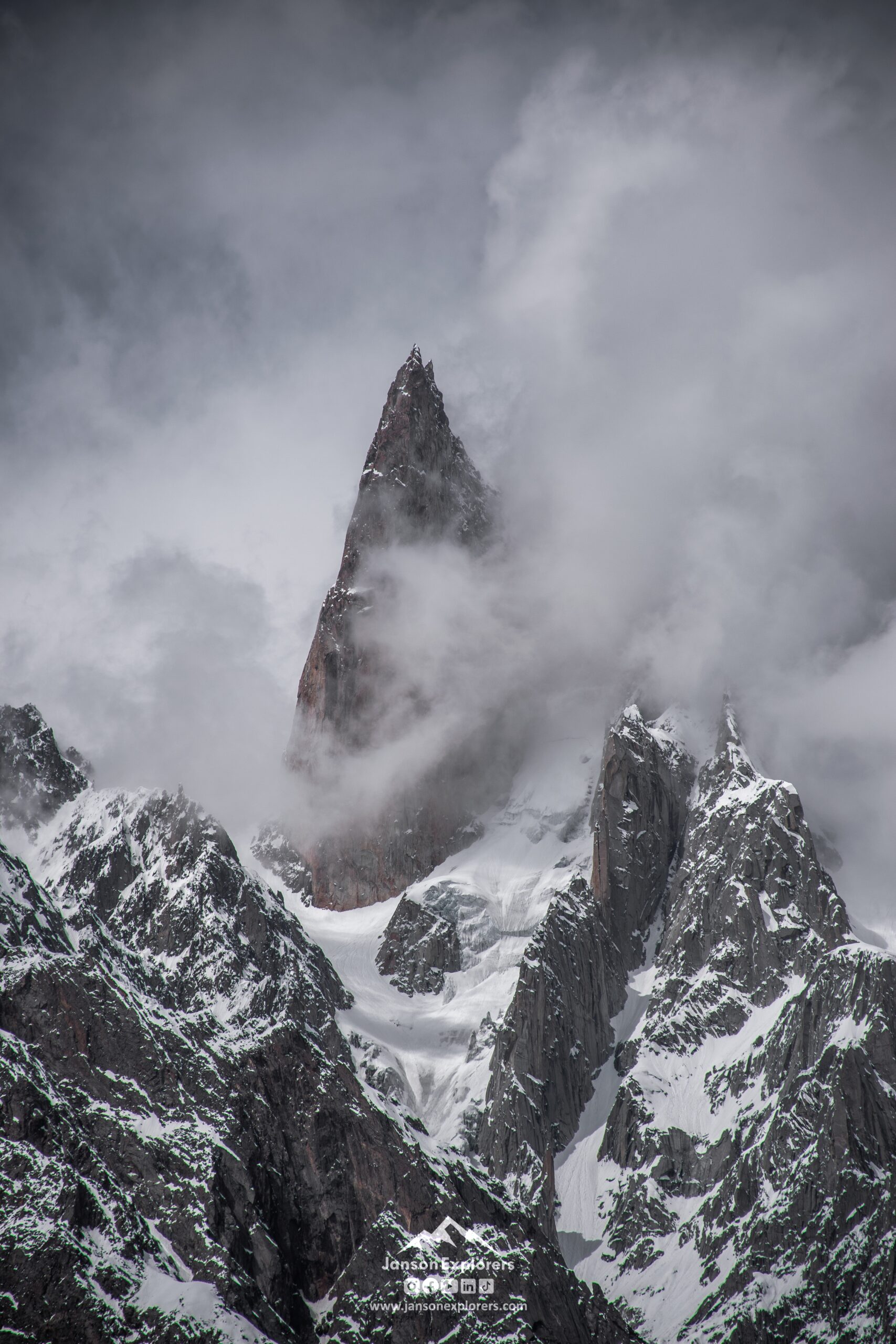 Passu Cones, Hunza—jagged mountain peak rising through clouds with snow-covered ridges and dramatic rocky cliffs.